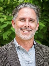 Joe Rhea, white male, grey hair, wearing a pale blue button-down shirt and herringbone sports jacket.